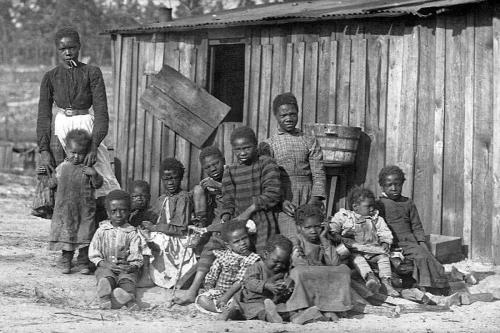 African American woman and twelve children stand outside a shed